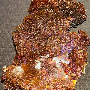 May include: A large, iridescent, layered piece of mica with a brown, gold, and purple color scheme. The mica is on a gray background.