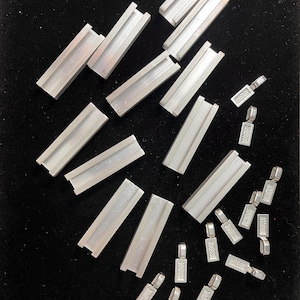 May include: A collection of silver metal jewelry findings, including rectangular and square shapes, and small, textured, rectangular charms.