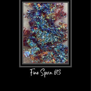May include: Close-up of iridescent blue, green, and red glitter flakes. The glitter is arranged in a loose, organic pattern. The text "Fine Spun 813" is printed below the glitter.