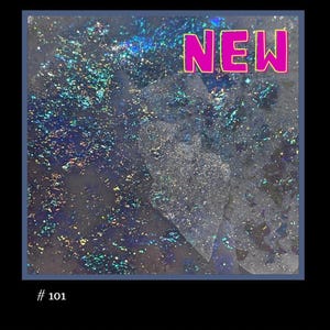 May include: A close-up of a glittery, iridescent blue and silver background with a white, translucent, geometric shape in the center. The word "NEW" is printed in pink letters at the top of the image.