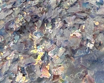 Puede incluir: Primer plano de escamas iridiscentes multicolores. Las escamas tienen una calidad brillante y reflectante, con tonos de azul, morado y dorado. El material parece fino y fragmentado, posiblemente para manualidades o fines decorativos.