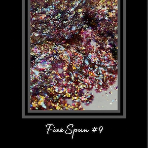 May include: Close-up of iridescent glitter with a variety of colors, including red, gold, and blue. The glitter is scattered on a white surface. Fine Spun #9