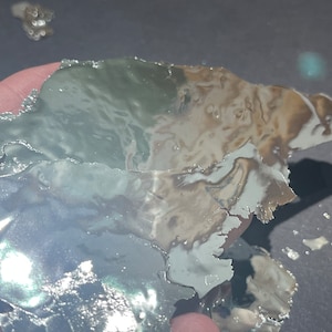 May include: A close-up of a piece of silver foil with a green and brown iridescent sheen. The foil is crumpled and has a textured surface.
