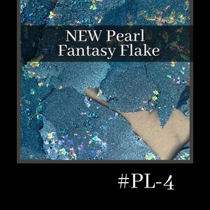 May include: Close-up of teal blue iridescent glitter flakes. The glitter is scattered on a brown surface. The text "NEW Pearl Fantasy Flake #PL-4" is printed below the glitter.