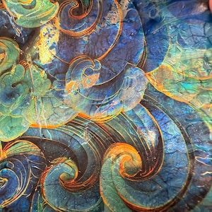 May include: A decorative glass plate featuring a swirling abstract pattern in deep blue, turquoise, and teal hues. The design incorporates intricate metallic gold linework that follows the curves of the waves, creating a textured, glossy surface.
