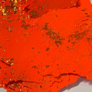 May include: Orange paper with gold glitter, torn and layered, creating a textured, abstract design.