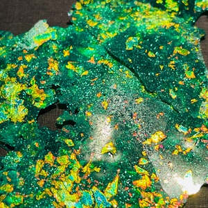 May include: Close-up of a green and gold iridescent glitter resin, with a textured, cracked surface.