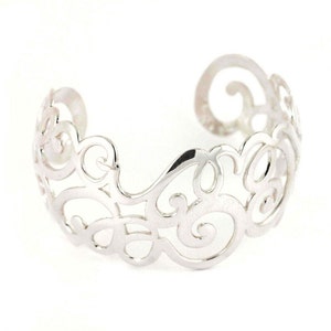 Könnte beinhalten: Ein silberfarbenes Armreif-Armband mit einem dekorativen, durchbrochenen Design. Das Armband weist eine Reihe von wirbelnden, scrollartigen Mustern auf, die einen filigranen und eleganten Look erzeugen. Das offene Design ermöglicht Flexibilität und Komfort.