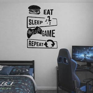 May include: A black and white wall decal with the words "EAT SLEEP GAME REPEAT" and a hamburger, a bed, a game controller, and a recycling symbol. A bed, computer, and gaming chair are in the room.
