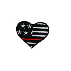 May include: A black and white heart-shaped patch with a red stripe across the middle. The patch features a stylized American flag design with white stars and stripes.