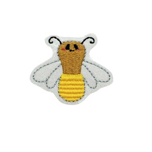 May include: A cute embroidered bee patch with a yellow and brown body and white wings. The bee has a smiling face with black eyes and pink cheeks.
