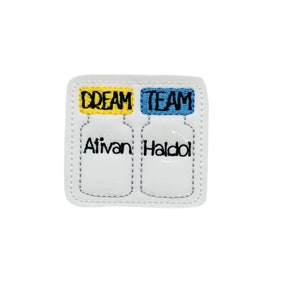 May include: A white patch with embroidered text and images of two medicine bottles. The top of each bottle is a different color, one yellow and one blue, with the words "DREAM TEAM" embroidered on top. The bottles are labeled "Ativan" and "Haldo".
