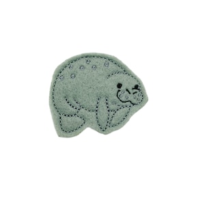 May include: A gray felt appliqué of a manatee with black embroidered eyes and a stitched smile.