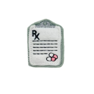 May include: A green felt patch with a white prescription pad and the letters "Rx" embroidered on it. Two pink and white pills are embroidered at the bottom of the pad.