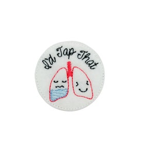 May include: White felt circle with red embroidered lungs, one with a blue face mask. The text "I'd Tap That" is embroidered around the lungs.