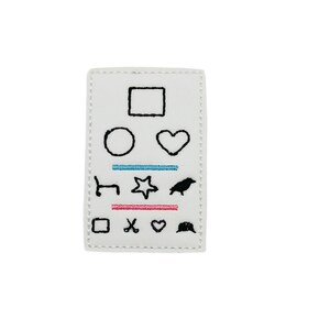 May include: White eye chart patch with black embroidered shapes including a square, circle, heart,  a horizontal line, a chair, a star, a bird, a square, scissors, a heart, and a hat.