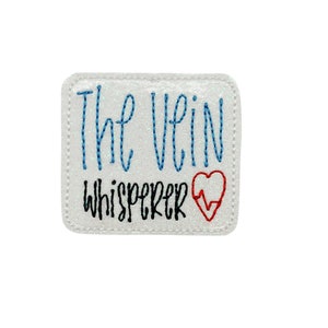 May include: White embroidered patch with blue text that reads "The Vein Whisperer" and a red heart with a heartbeat symbol.