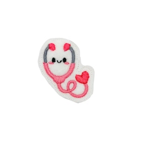 May include: A white felt patch with an embroidered pink stethoscope with a cute cartoon face. The stethoscope has a gray earpiece and a red heart at the end of the tube.