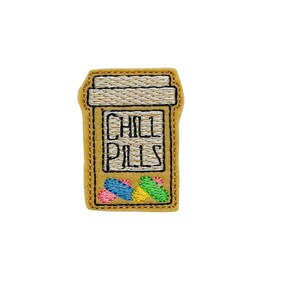 May include: Embroidered patch of a pill bottle with the text "CHILL PILLS" and colorful pills inside. The patch is beige with white stitching.