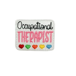 May include: White embroidered patch with the text "Occupational Therapist" in pink lettering and black outline. Five small rainbow hearts are below the text.