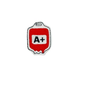 May include: Red embroidered patch shaped like a blood bag with a white background and black outline. The bag has a black label with the text "A+" in white.