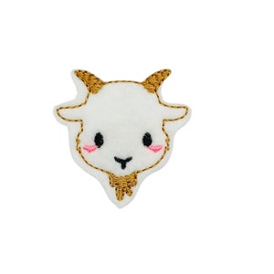 May include: White felt applique of a goat's face with gold embroidered horns, eyes, nose, and beard. The goat has pink cheeks.