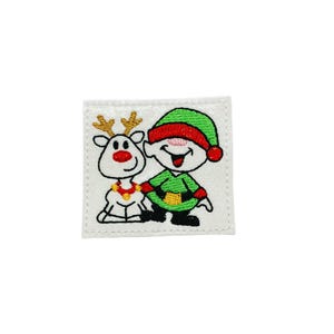 May include: Embroidered patch featuring a cartoon reindeer and elf. The reindeer has gold antlers and a red nose, while the elf wears a green outfit and hat with a red brim. The patch is square and has a white background.