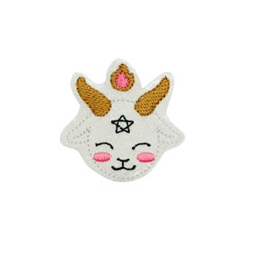 May include: White felt patch with a cute cartoon goat face. The goat has pink cheeks, a black nose, and a gold star on its forehead. The goat's horns are gold.