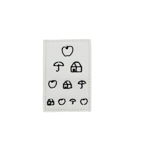 May include: White eye chart with black embroidered symbols, including an apple, umbrella, and house.