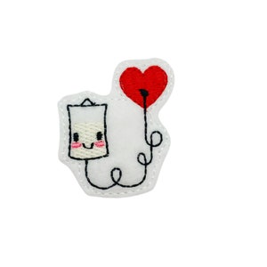 May include: Embroidered felt patch with a white IV bag with a smiling face and a red heart balloon attached to it.