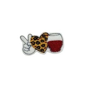 May include: Embroidered iron-on patch with a peace sign holding a heart-shaped glass of wine with a leopard print design.