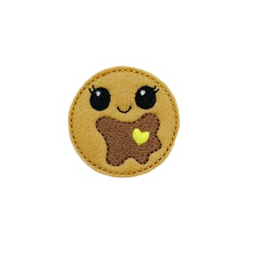 May include: A brown felt cookie with a smiling face, big eyes, and a brown chocolate star with a yellow heart on top.