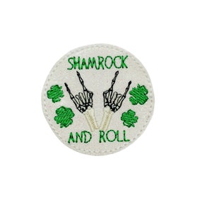 May include: White round patch with green shamrocks and two skeleton hands making the rock and roll sign. The text "Shamrock and Roll" is embroidered on the patch.