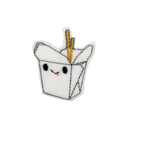 May include: White felt embroidered patch of a cartoon takeout container with a smiling face and chopsticks sticking out of the top.