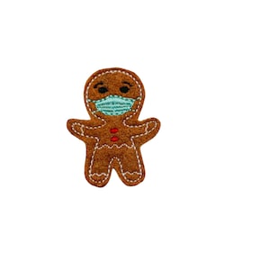 May include: A brown gingerbread man wearing a blue face mask. The gingerbread man has red buttons and black eyes.