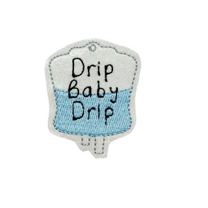 May include: White and blue embroidered iron-on patch shaped like an IV bag with the text "Drip Baby Drip".