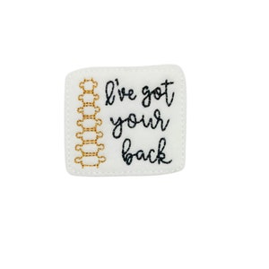 May include: White felt patch with gold embroidered spine and black embroidered text that reads "I've got your back".