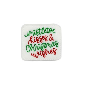 May include: White felt square with green and red embroidered text that reads "mistletoe kisses & christmas wishes".