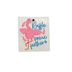 May include: Pink flamingo embroidered iron-on patch with the text "Ruffle some feathers" in blue thread on a white background.