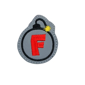 May include: A gray embroidered patch shaped like a bomb with a black fuse and a yellow spark. The bomb has a red letter "F" inside.