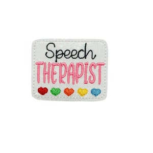 May include: White iron-on patch with pink glitter and the text "Speech Therapist" in black and pink lettering.  Five small rainbow hearts are below the text.