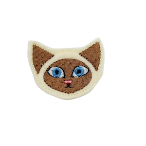 May include: A white felt cat face with brown ears and a brown nose. The cat has blue eyes.
