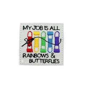 May include: White embroidered patch with the text "My job is all rainbows & butterflies". The patch features a needle and thread with rainbow colored spools of thread.