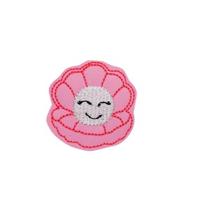 May include: Pink embroidered patch with a smiling face in the center, resembling a seashell.