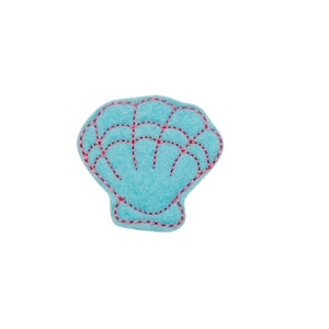 May include: A light blue felt seashell with pink and red embroidered details. The seashell shape is outlined with pink thread, and the interior features a grid pattern in red thread. The background is white.