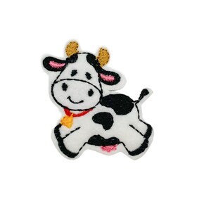 May include: A white and black embroidered patch of a cartoon cow with a red collar and a gold bell. The cow has pink ears and gold horns.