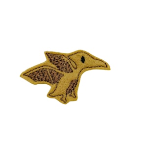 May include: A brown felt embroidered patch of a pterodactyl with brown wings and a black eye.