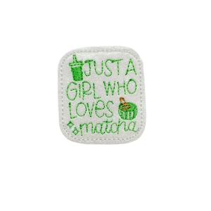 May include: A white, rectangular patch with a glittery border, embroidered with green thread. The text reads "JUST A GIRL WHO LOVES matcha", accompanied by a matcha drink and a matcha dessert illustration.