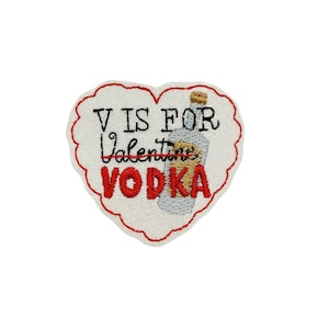 May include: Embroidered heart-shaped patch with the text "V IS FOR Vodka" in black and red. A vodka bottle is embroidered on the right side. The patch has a white glittery background and a red scalloped border.