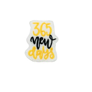 May include: A white felt patch with yellow embroidered text that reads "365 new days".